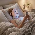 Vrouw ontspant in bed met het draadloze ERAYS. LED Skincare Glow Masker en nek-module tijdens haar avondroutine.